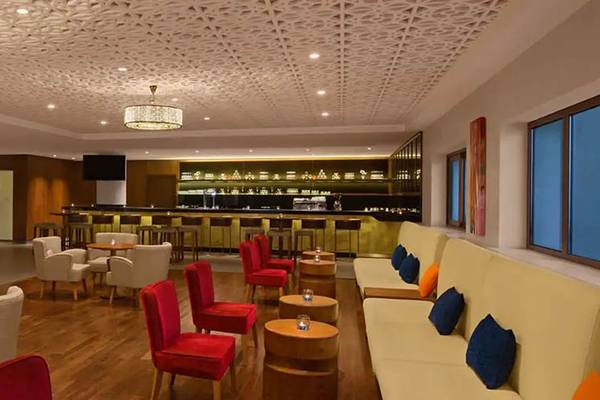 Loungebereich des DoubleTree by Hilton Resort & Spa Marjan Island mit weißen und roten Stühlen, Tischen und einer Bar.