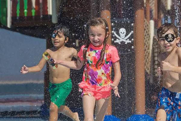 Drei Kinder laufen durch Wasserspritzer im Wasserpark des DoubleTree by Hilton Resort & Spa Marjan Island.