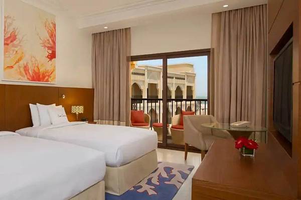 Doppelzimmer im DoubleTree by Hilton Resort & Spa Marjan Island mit zwei Betten, Kunstwerken an der Wand, Balkon und moderner Einrichtung.