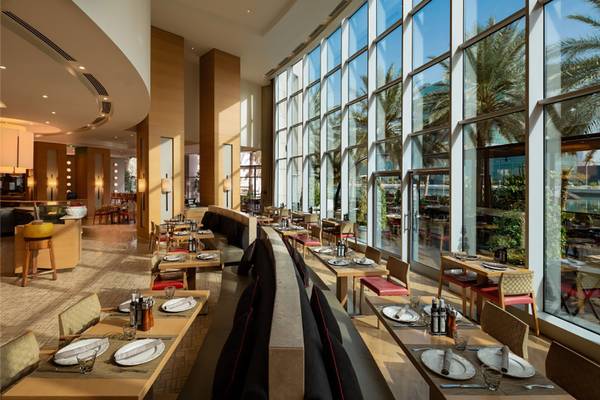 Innenansicht des Restaurants im Beach Rotana Hotel mit runden Tischen und hohen Fenstern.