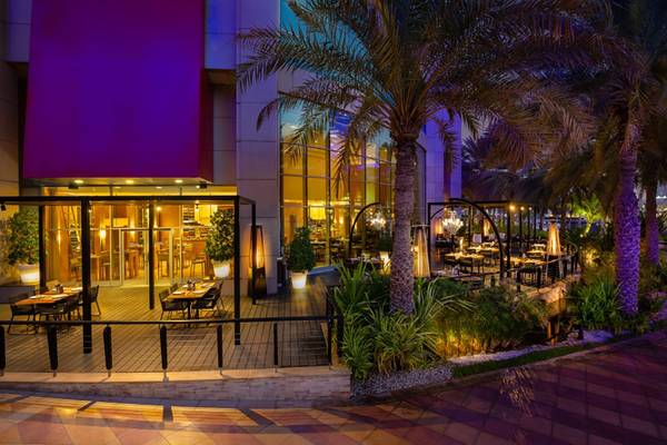 Außenbereich des Beach Rotana Hotels mit abendlicher Beleuchtung und Tischen im Freien.