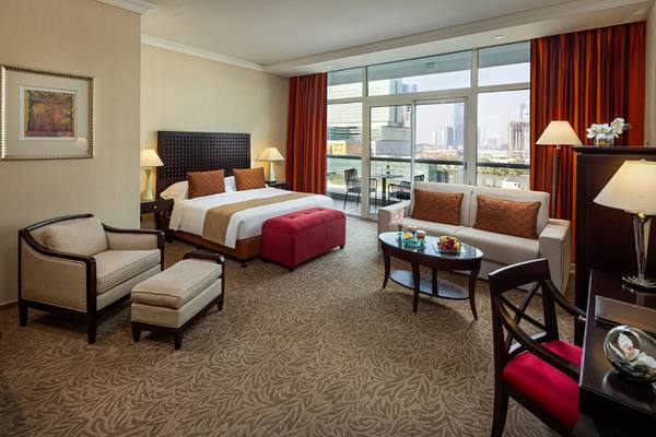 Innenansicht eines Hotelzimmers im Beach Rotana mit Bett, Wohnzimmerbereich und Blick auf die Stadt.