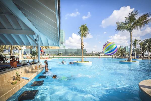 Ein Schwimmbecken im Beach Rotana Hotel mit badenden Personen und Palmen im Hintergrund.