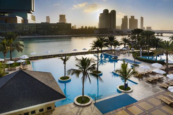 Überblick über den Poolbereich des Beach Rotana Hotels mit Palmen und Sonnenschirmen.
