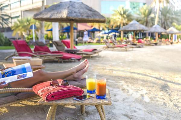 Personen entspannen auf Liegen am Strand im Beach Rotana Hotel