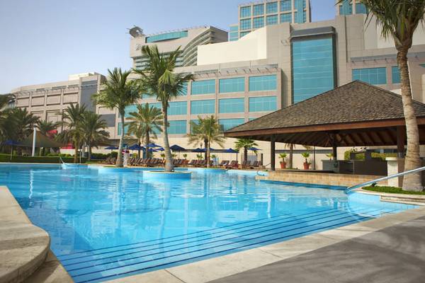 Ein großer Swimmingpool vor dem Beach Rotana Hotel mit vielen Sonnenliegen und Palmen.