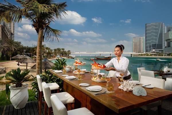 Frau serviert Essen auf der Terrasse des Beach Rotana Hotels mit Blick auf den Strand und die Stadt.