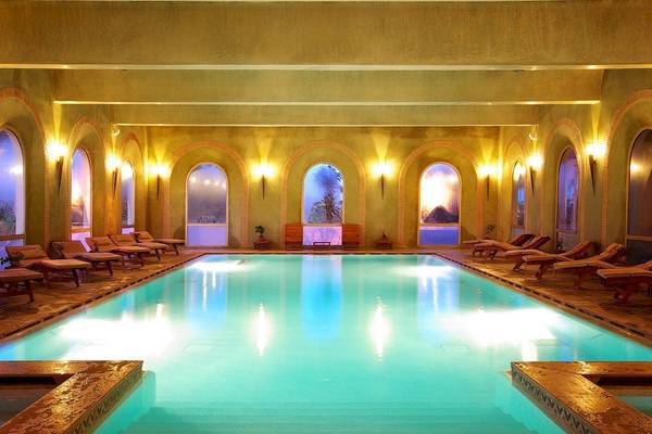 Der Poolbereich des Palmeraie Palace Hotels mit Lounge-Liegestühlen und beleuchteten Wänden.