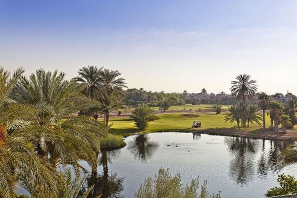 Aussicht auf den Golfplatz des Palmeraie Palace mit einem Golfwagen und einem See.