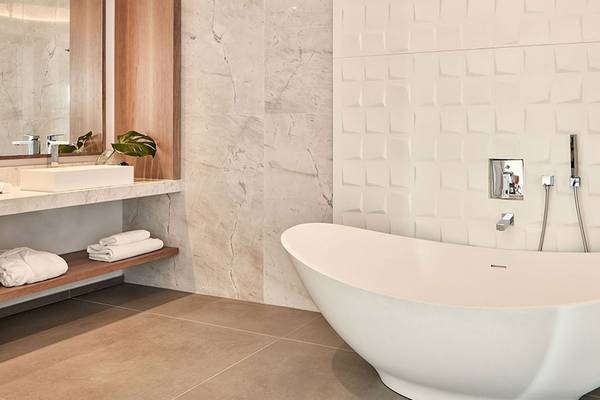 Ein Badezimmer mit einer freistehenden weißen Badewanne und gemusterten weißen Fliesen an der Wand.