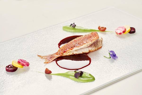Fischgericht mit Beilagen auf einem Glasteller im Myconian Korali Relais & Chateaux