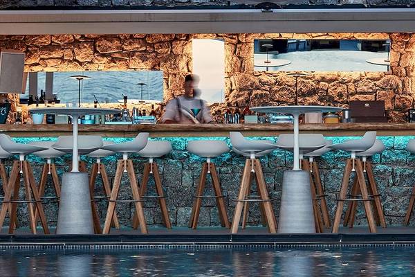 Poolbar des Myconian Korali Relais & Chateaux Hotels mit Steinwand und weißen Stühlen.