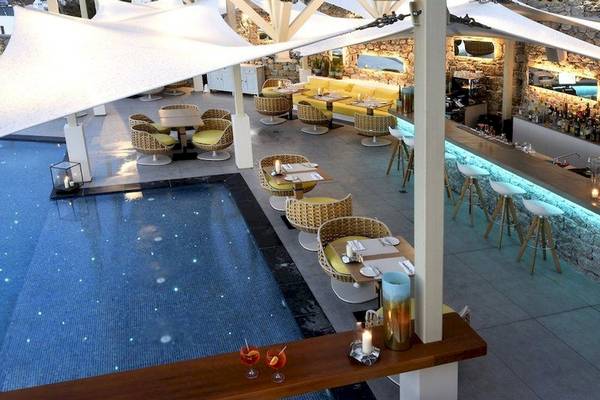 Pool-Lounge des Myconian Korali Hotels mit Tischen, Stühlen und Bar.