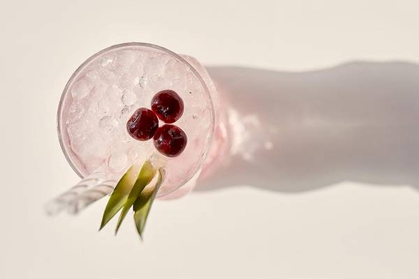 Cocktail mit Eis, roten Beeren und grünem Gras im Glas mit Schatten auf weißer Oberfläche