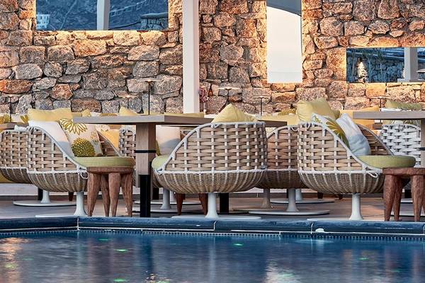 Sitzecke am Pool des Myconian Korali Relais & Chateaux Hotels mit Steinwand und weichen Kissen.