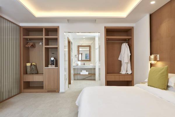 Innenansicht eines Schlafzimmers im Myconian Korali Hotel mit Bett, Nachttisch und offenem Kleiderschrank.