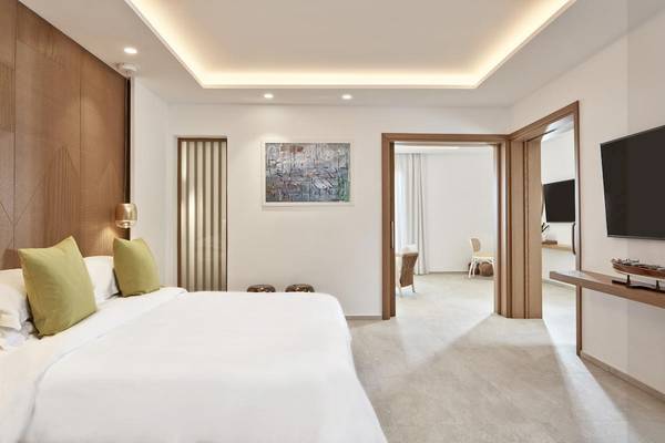 Innenansicht eines Schlafzimmers im Myconian Korali Relais & Chateaux Hotel, mit einem großen Bett, grünen Kissen, einem Fernseher und einer modernen Einrichtung.