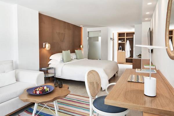 Hotelzimmer von Myconian Korali Relais & Chateaux mit Bett, Couch, Tisch und buntem Teppich.