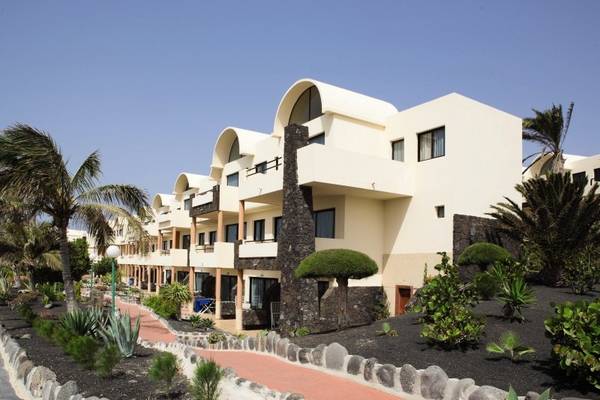 Außenansicht des SBH Royal Monica Hotels mit weißen Gebäuden und schwarzen Gartenbeeten.