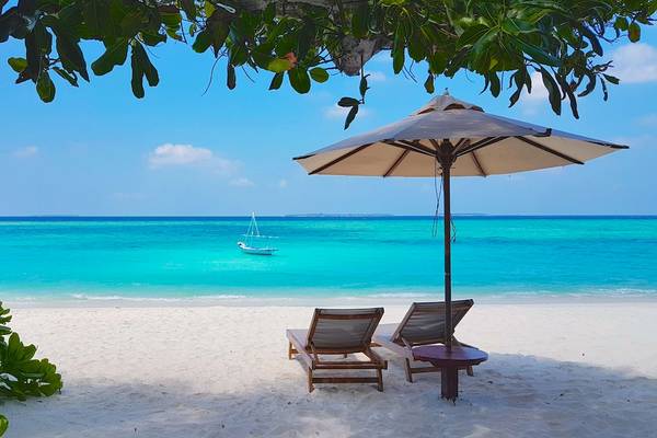 Strand mit Sonnenschirm, zwei Liegen und einem Boot im Wasser