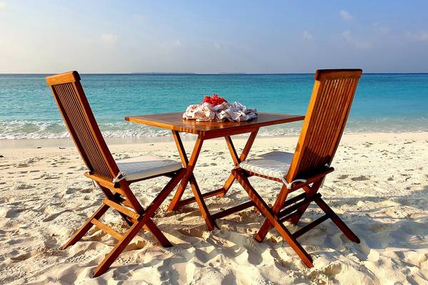 Ein Holztisch am Strand des Barefoot Eco Hotels mit zwei Stühlen und Blick auf das Meer.