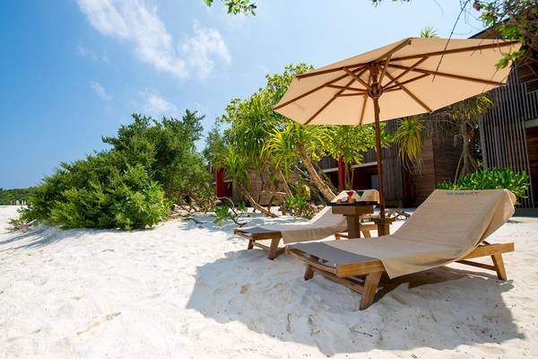 Zwei Sonnenliegen auf dem weißen Sandstrand des Barefoot Eco Hotels mit einem Schirm