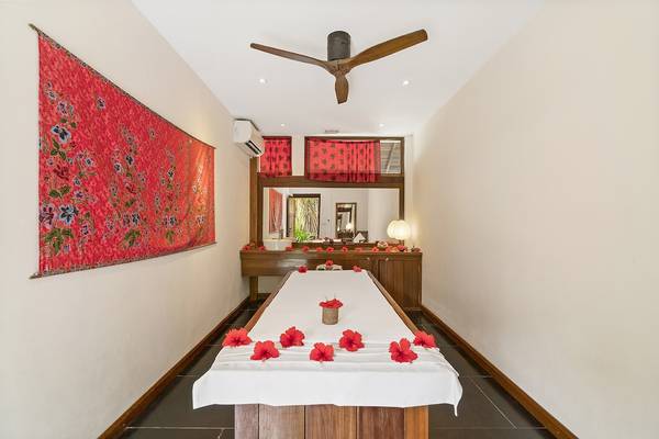 Innenansicht des Massageraums im Barefoot Eco Hotel mit weißem Tisch, roten Blumen und Wanddekoration.