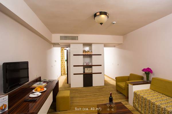 Innenansicht der Suite im Defne Star Hotel mit Fernseher, Obstteller, Weinflasche, Sofas und Schreibtisch.