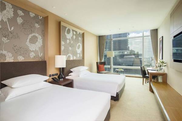 Zwei Doppelbetten in einem Hotelzimmer des Eastin Grand Hotel Sathorn mit Blick auf die Stadt.