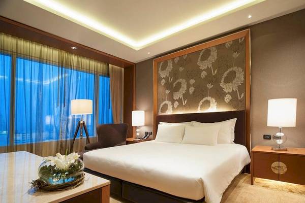 Schlafzimmer im Eastin Grand Hotel Sathorn mit großem Bett, Nachttischen und Schreibtisch.