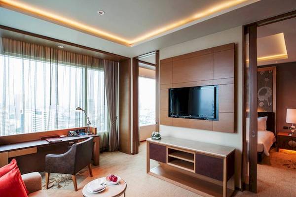 Innenansicht der Suite im Eastin Grand Hotel Sathorn mit Schreibtisch, Fernseher und Blick auf die Stadt.