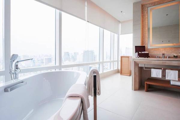 Badezimmer im Eastin Grand Hotel Sathorn mit Badewanne, Spiegel und Fenstern mit Stadtblick.