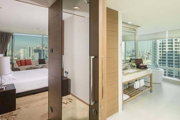 Innenansicht eines Zimmers im Eastin Grand Hotel Sathorn mit Bett, Sofa, Schreibtisch und Aussicht auf die Stadt.