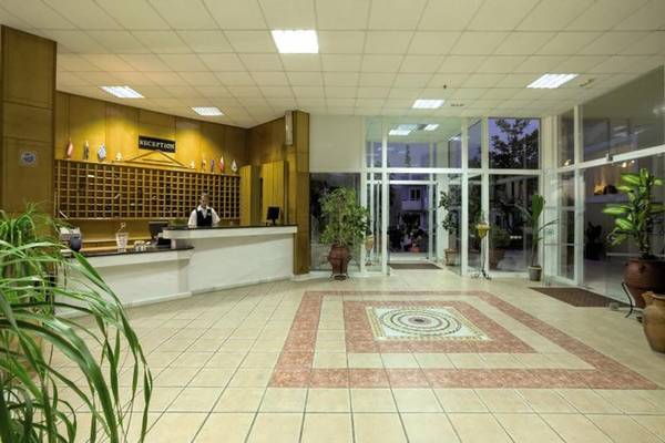 Empfangsbereich des Corali Hotels mit Rezeption, Pflanzen und gefliestem Boden.