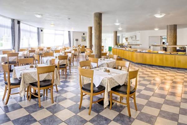 Innenbereich des Corali Hotel Restaurants mit gedeckten Tischen und Stühlen auf einem Schachbrettmusterboden.