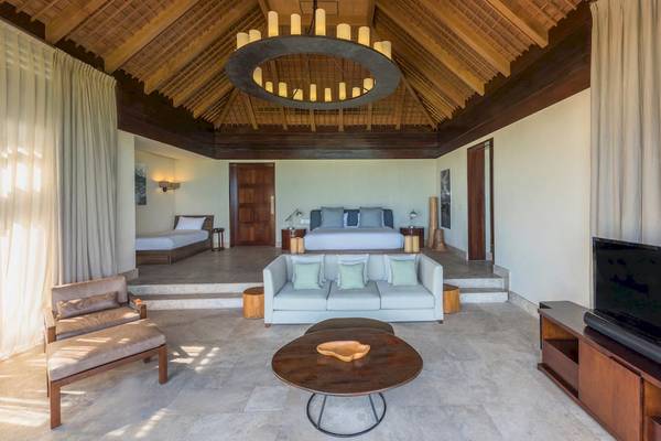 Innenansicht einer Suite im JW Marriott Mauritius Resort mit einem Wohnzimmer, einem Bett, einem Couchtisch und einer Fernsehwand.
