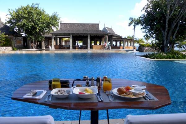 Frühstückstisch am Pool im JW Marriott Mauritius Resort mit Blick auf das Hotelgebäude und den Swimmingpool.