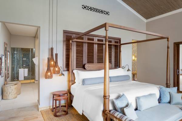 Innenansicht des Schlafzimmers im JW Marriott Mauritius Resort mit einem vierposterbett, hängenden lampen und einem offenen eingang.