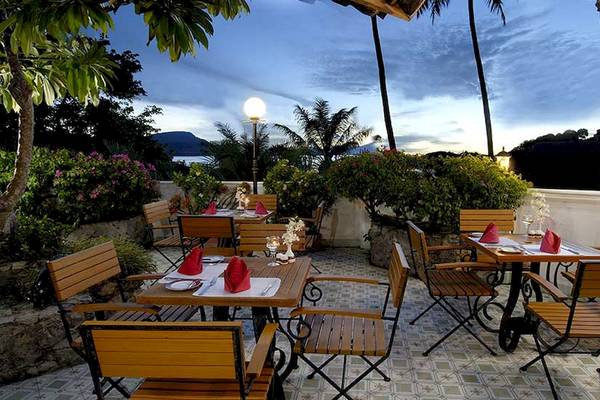 Außenterrasse des Cape Panwa Hotels mit gedeckten Tischen und Stühlen bei Sonnenuntergang.