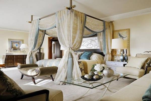 Luxuriöses Schlafzimmer im Palace At One & Only Royal Mirage mit einem Baldachinbett, einem Glastisch, Sesseln und Lampen.