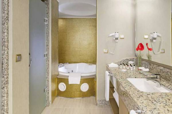 Ein Badezimmer im Royal Holiday Palace mit einem goldenen Whirlpool, einer Marmortheke und einem Spiegel.