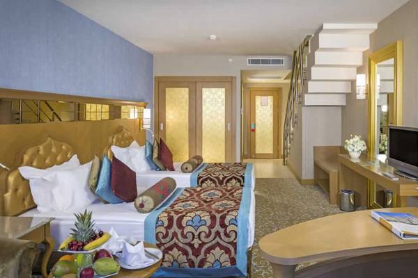 Innenansicht eines Hotelzimmers im Royal Holiday Palace mit zwei Betten, Früchten auf einem Tisch und einem Fernseher.