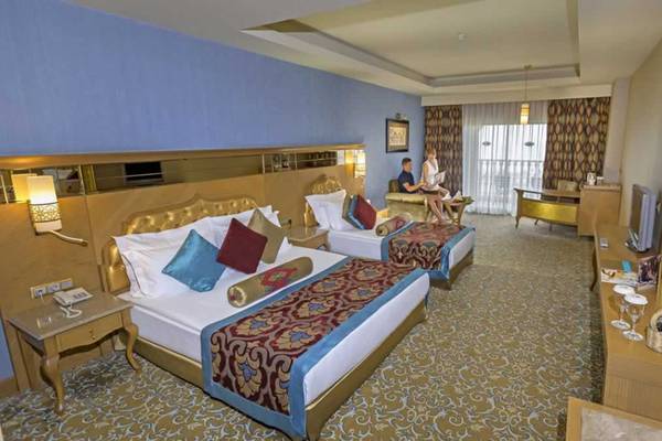 Ein Hotelzimmer des Royal Holiday Palace mit zwei Betten, einem Balkon und zwei Personen, die auf einem Balkon sitzen.