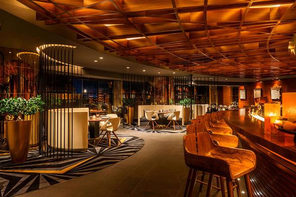 Innenbereich des Le Royal Meridien Beach Resort & Spa mit holzigen Decken, Esstischen und Barhockern.