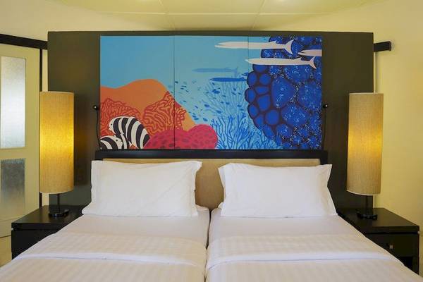 Doppelbett-Zimmer im Angsana Velavaru mit farbenfrohem Wandbild und zwei Nachttischen mit Lampen.