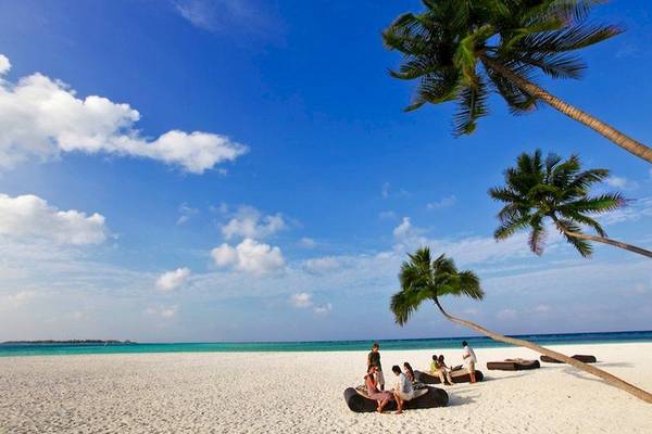 Strand mit weißen Palmen und einigen Personen, die auf Liegen sitzen, am Angsana Velavaru