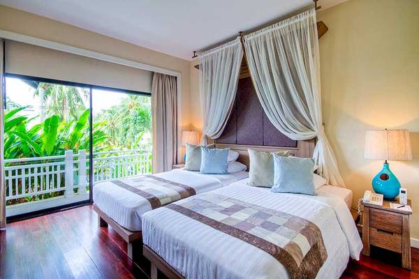 Doppelzimmer im Cape Panwa Hotel mit zwei Betten, Vorhängen und Balkon mit Blick auf Pflanzen.