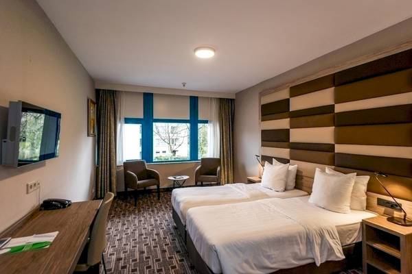 Doppelzimmer im XO Hotels Blue Square mit zwei Betten, Fernseher, Schreibtisch und Fenstern.