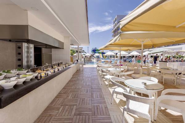 Terrasse im Glamour Resort & Spa mit Speisen, Tischen und Stühlen und Pool im Hintergrund.