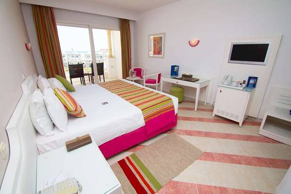 Innenansicht eines Schlafzimmers im Golden Tulip Taj Sultan Hotel mit Bett, Fernseher und Balkonzugang.